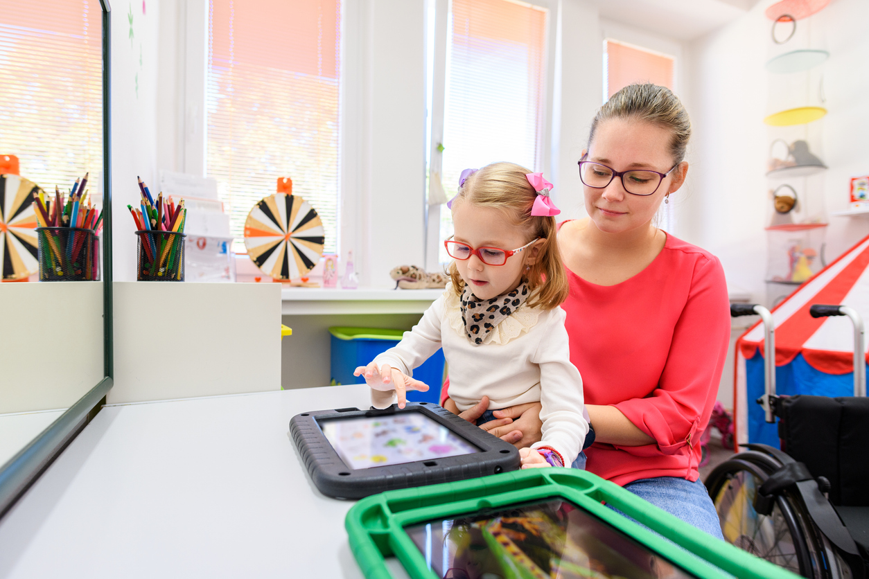 A special education teacher helps a nonverbal student use a tablet to communicate.