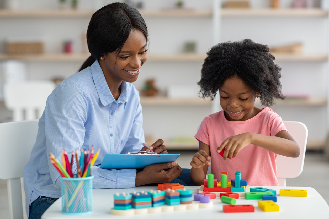 A child development specialist takes notes while a student works with manipulables.